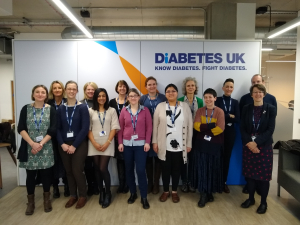 Photo of 14 members of the steering group in front of a Diabetes UK banner