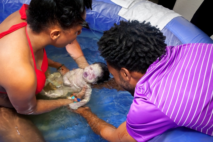 <p>Image of an African-American couple delivering their newborn in a birthing pool
