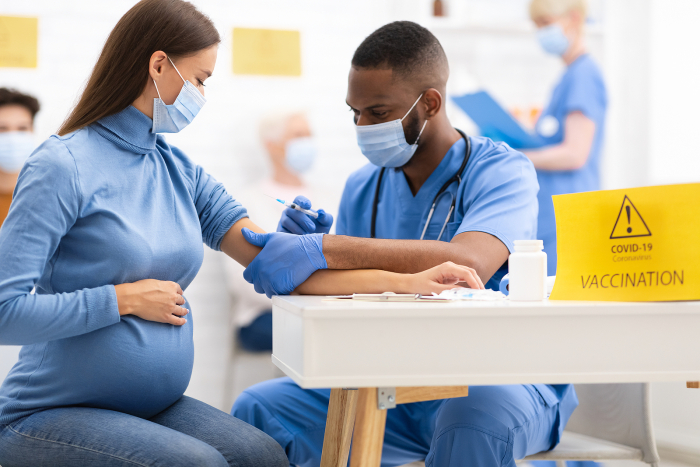 <p>Pregnant women receiving a Covid vaccine from a doctor.
