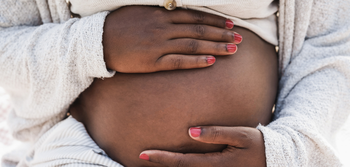 <p>Close up of a pregnant woman with hands on her stomach.
