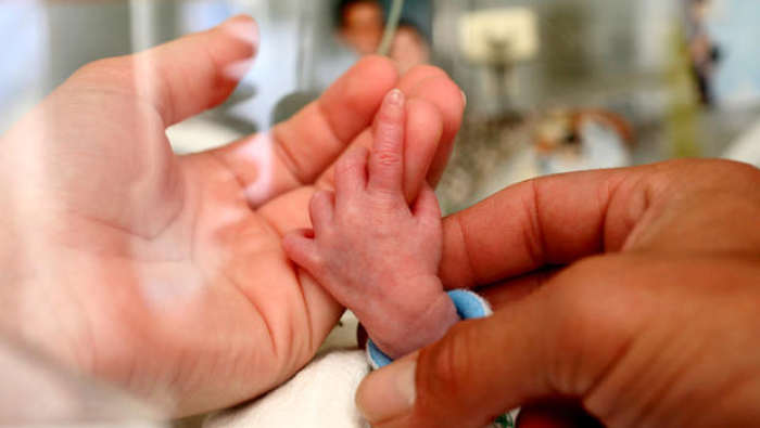 <p>Parents hold the hand of a premature baby in hospital
