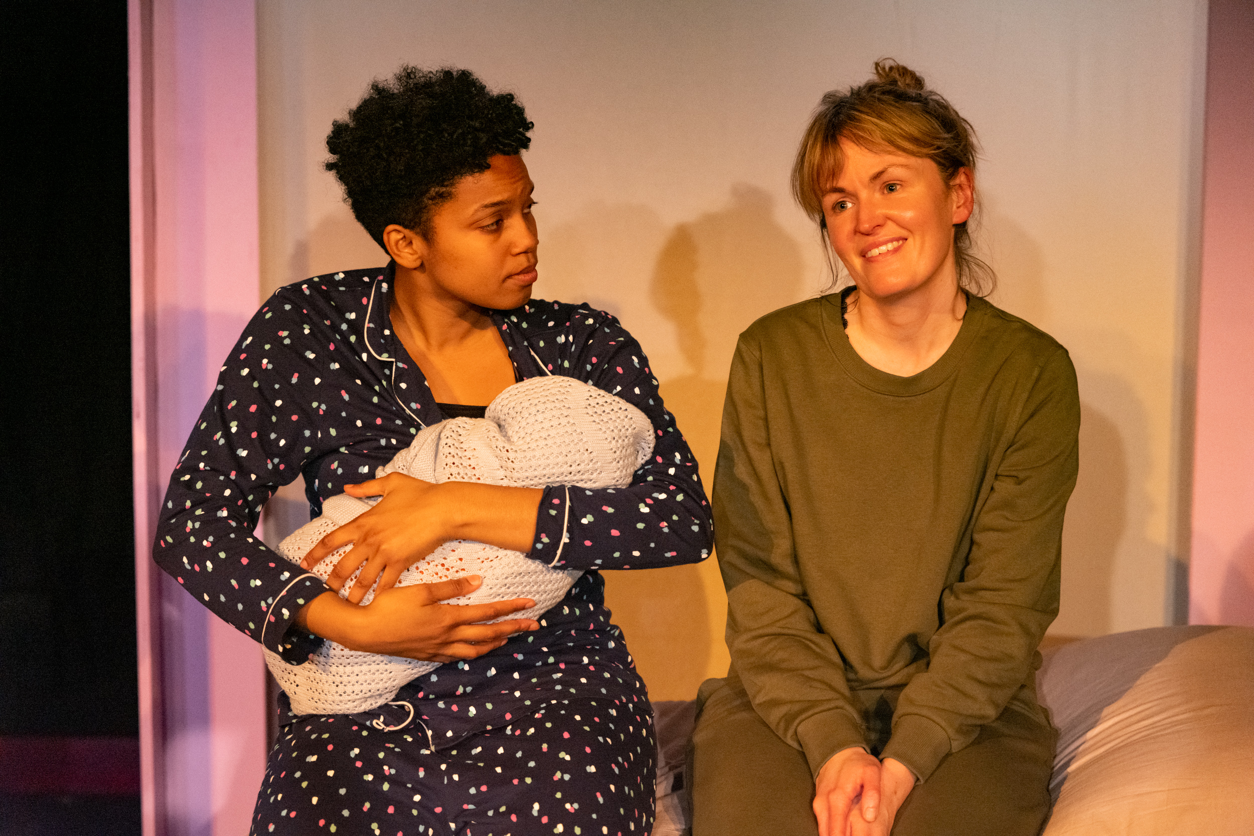 Actors from the After Birth play - two women talking, one is holding a baby.
