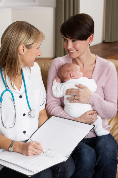 <p>A smiling mother holds her newborn whilst listening to a doctor
